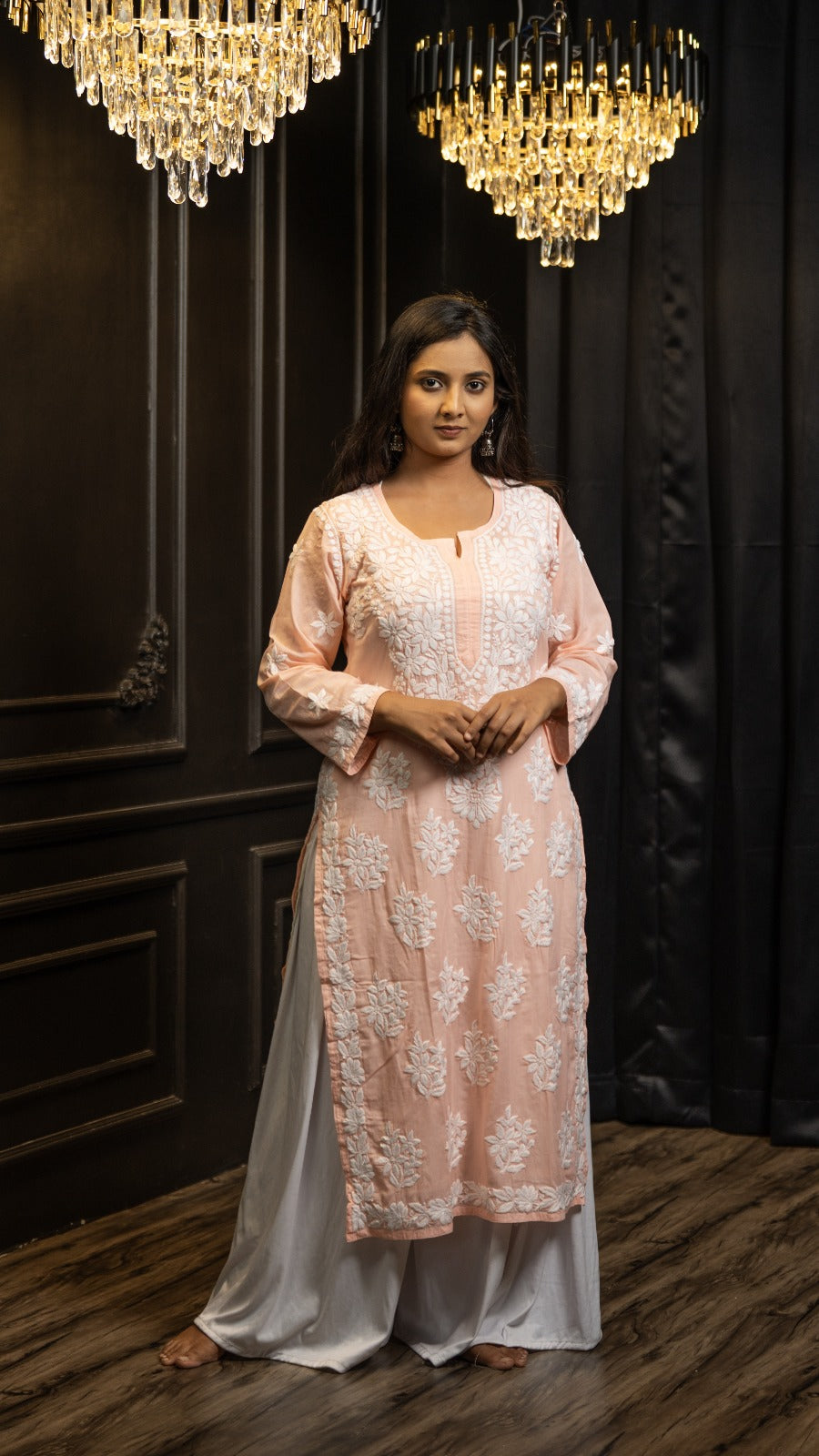 Woman wearing a light pink and white traditional outfit with a dark background